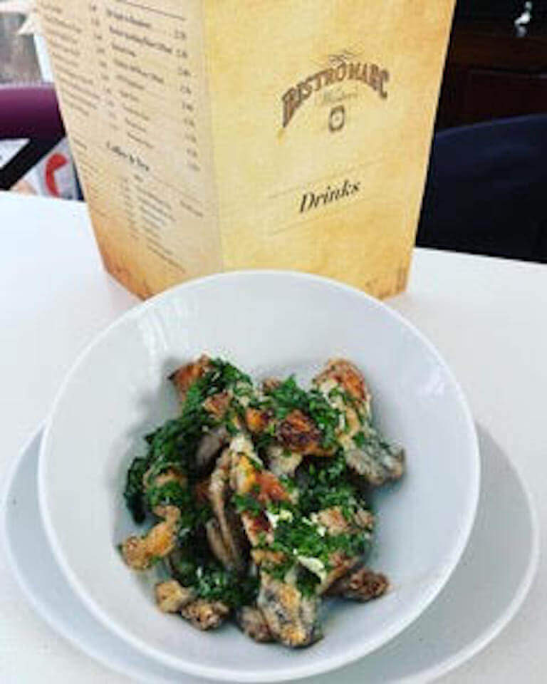 A bowl of pan-fried frogs with salsa verde seasoning in front of a Bistro Marc drinks menu.