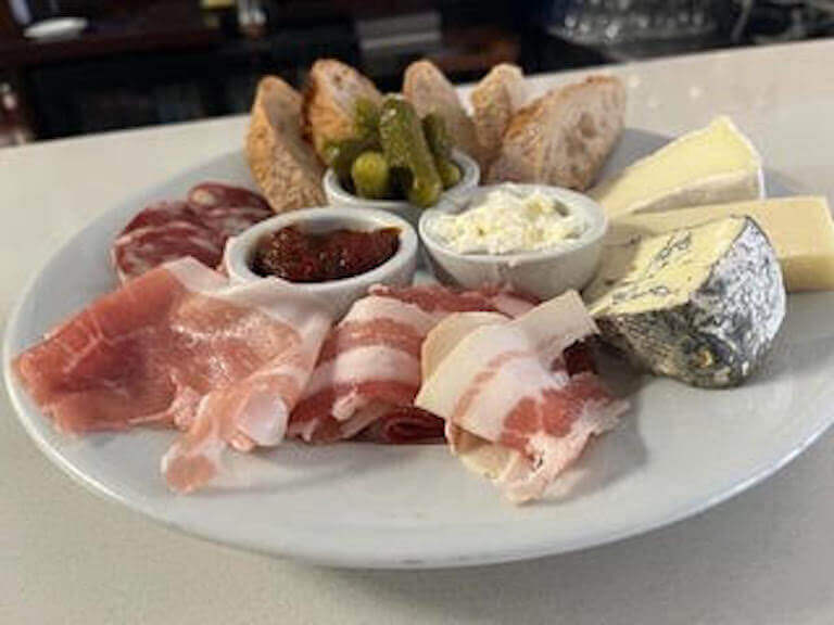 A charcuterie board with cured meats, cheeses, bread, and pickles, arranged on a white plate.