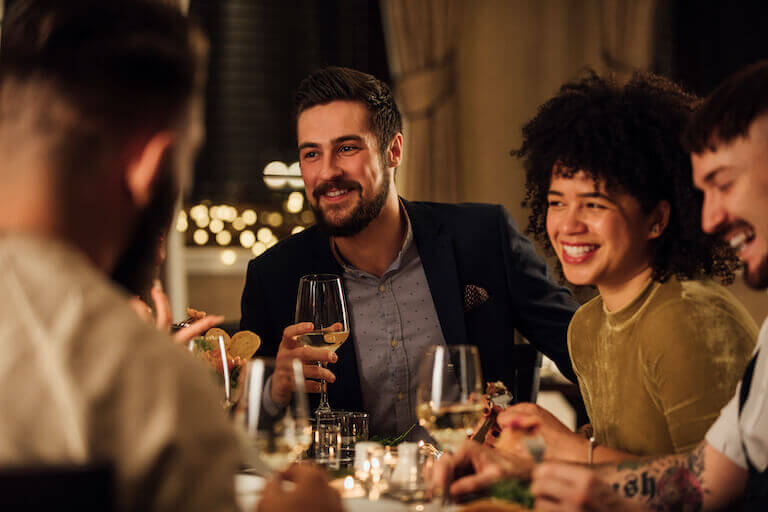 A well-dressed group of friends enjoys a lively dinner in a warmly lit restaurant.