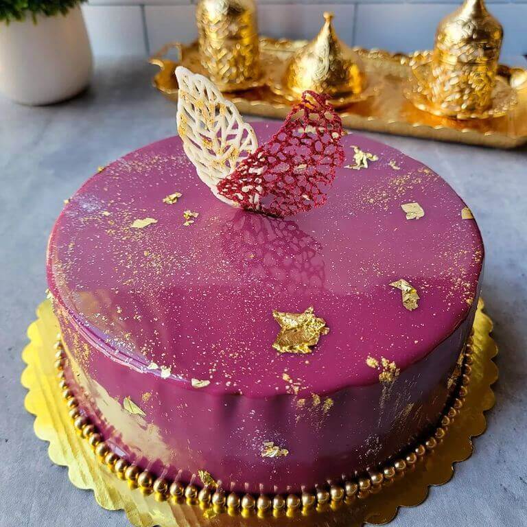 A maroon mirror glaze finish cake with gold accents made by and Escoffier student