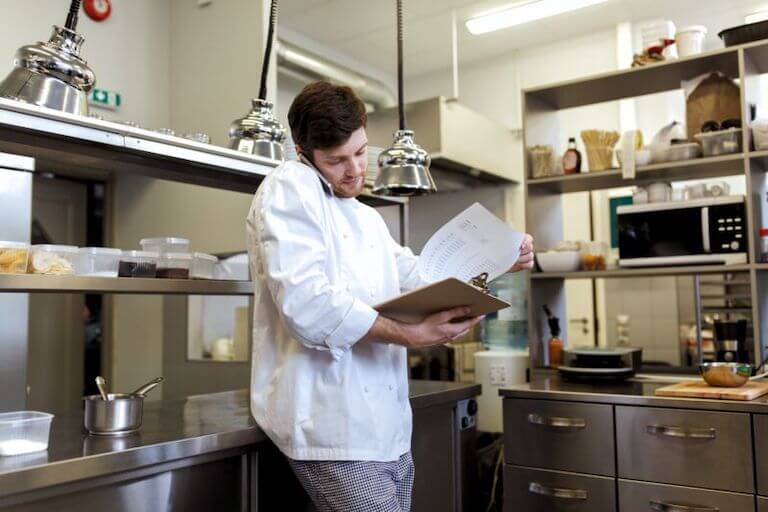 A person in a chef uniform using a clipboard for inventory management.