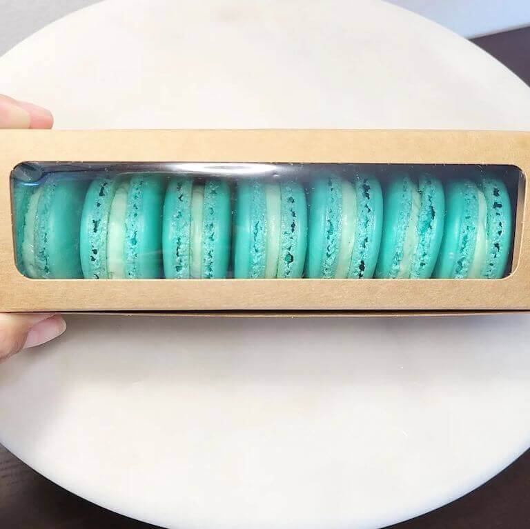 A row of neatly arranged blue vanilla macarons lined up in a bakery box.