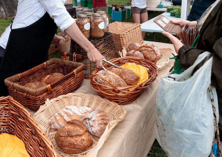 A long folding table covered in a tan tablecloth, with baskets of loaves of bread.