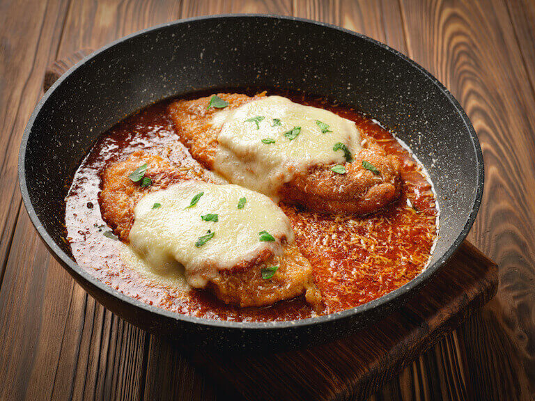 Black frying pan with two chicken parmesan cutlets.