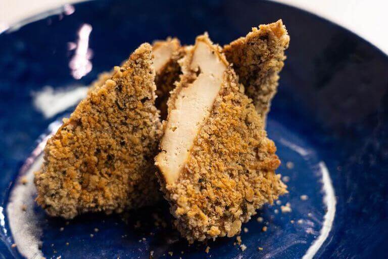 Breaded tofu cut in half on a blue plate