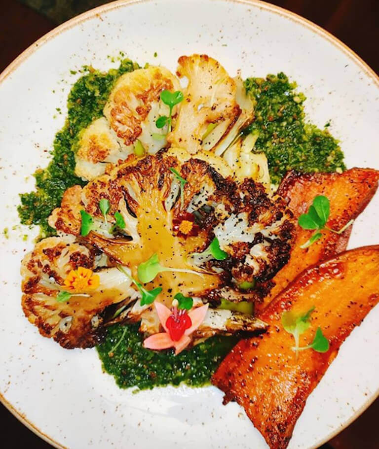 Cauliflower steak served on a white plate, garnished with herbs and drizzled with sauce.