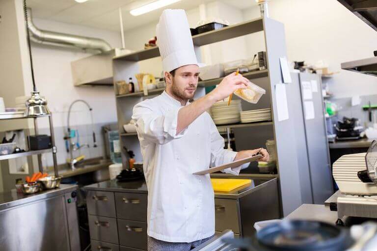 A chef holds up a plastic container and reads the label to check the date.