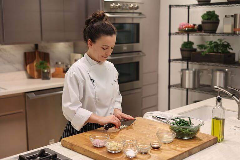 Chef chopping garlic on a large wooden cutting board.
