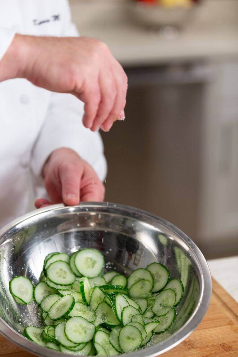 Chef salting pickles in a metal bowl