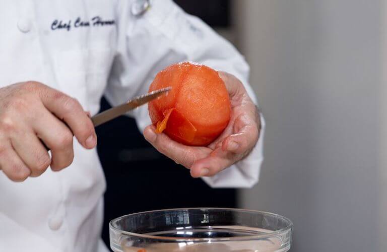 Chef using a knife to peel the skin from a tomato.