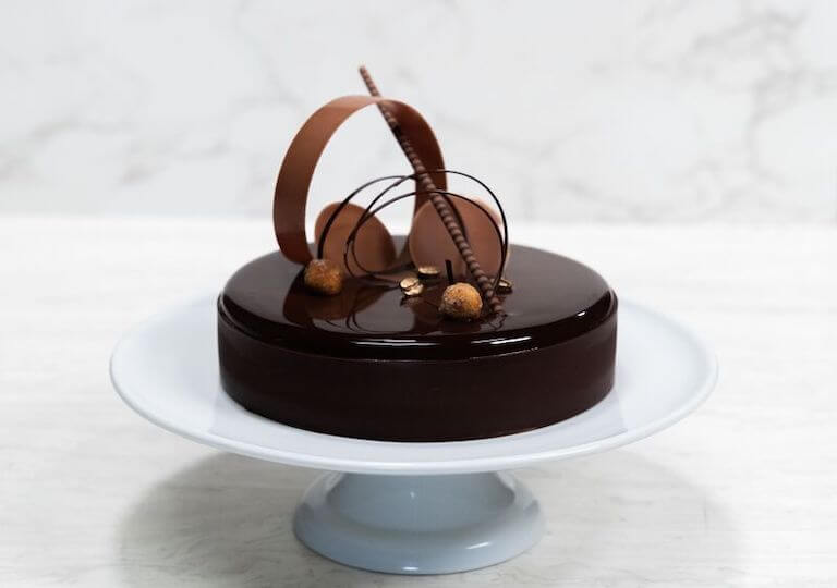 Chocolate entremet cake with elegant layers and a glossy finish, displayed on a white cake stand against a neutral background.
