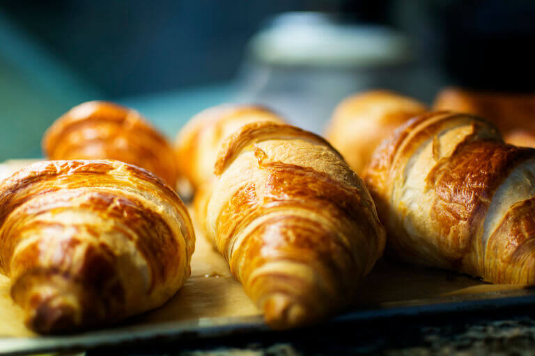 A close-up photo shows a line of perfectly browned, flaky croissants.