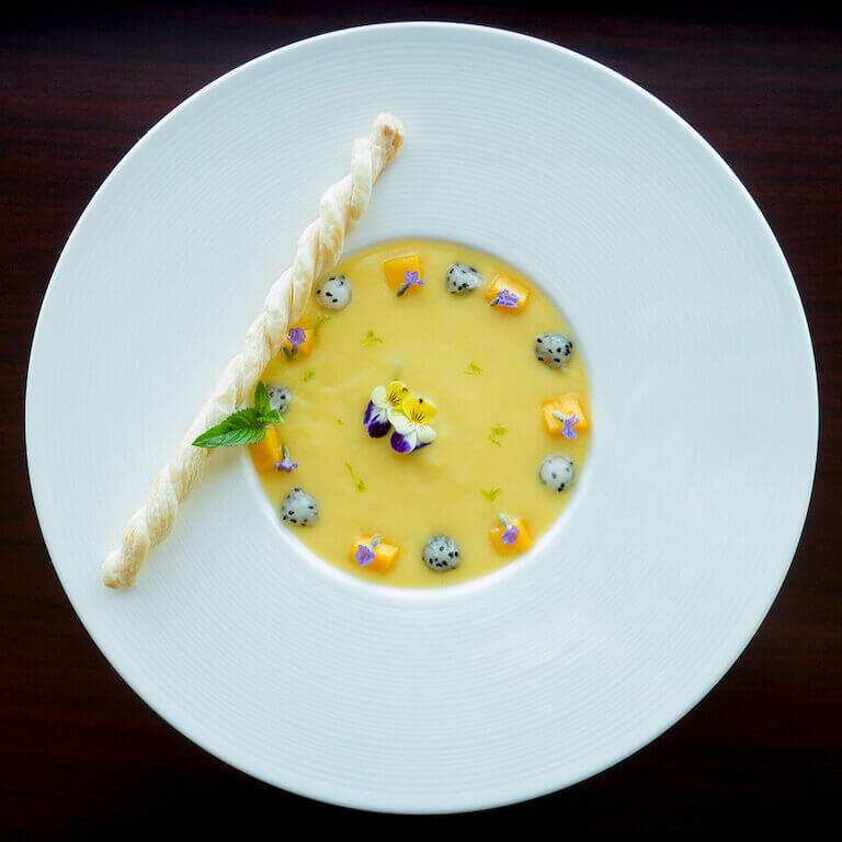 Cold fruit soup garnished with flowers in a white bowl
