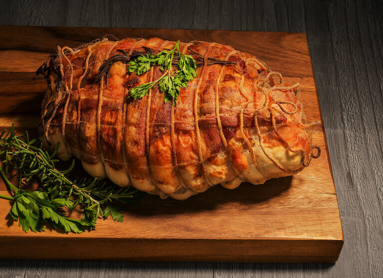 Whole cooked turducken resting on a wooden cutting board, showcasing the layered technique of engastration with turkey, duck, and chicken.