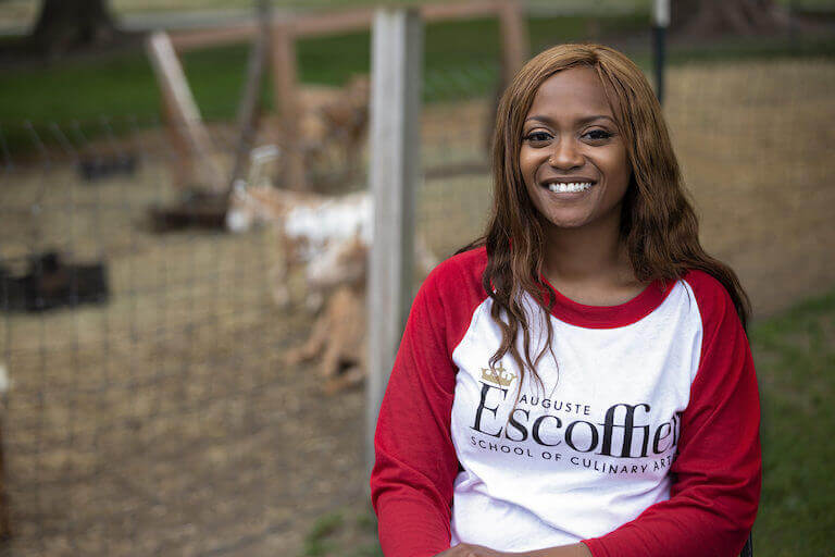 Culinary student sitting outside wearing a red and white shirt with the Escoffier logo