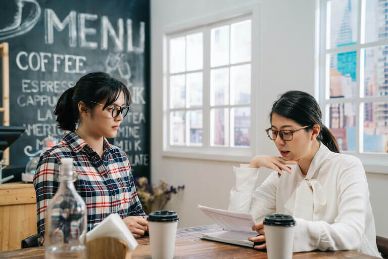 Employee wearing a white shirt and glasses looking at papers while sitting across from woman in a plad shirt