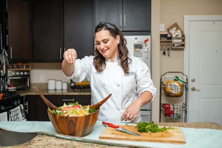 Escoffier student Lisa adding seasoning to a salad in a wood bowl