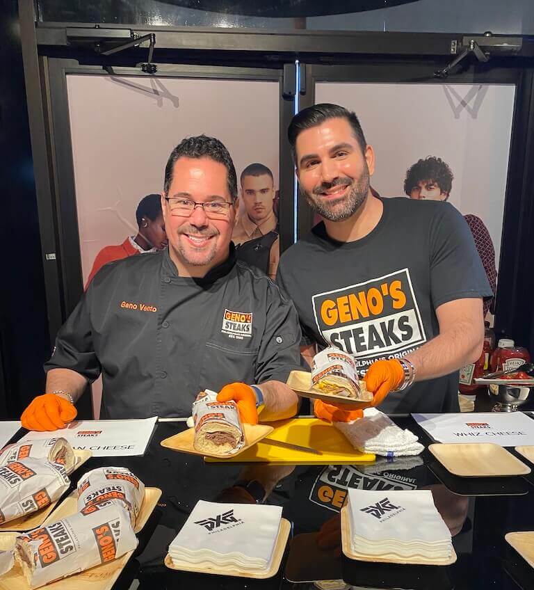Geno Vento and husband, Andre Gaspar, hand a wrapped Philly cheesesteak sandwich to a customer.