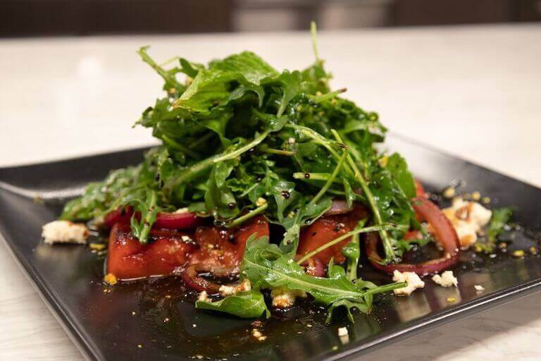Grilled watermelon dish topped with lettuce on a white plate