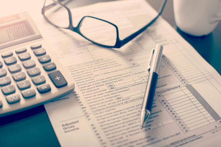 A pen, a pair of glasses, and a calculator sit on top of a blank tax form.