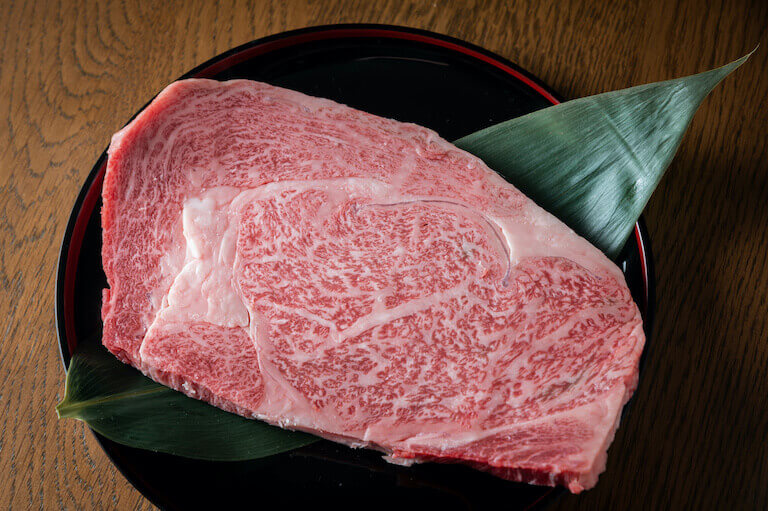 A raw piece of Kobe beef sits on a black plate. It has the distinctive marbling that distinguishes this type of meat.
