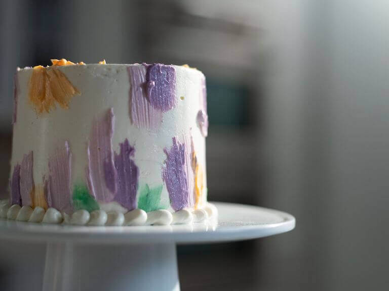 Layer cake decorated with pastel-colored frosting in soft hues of pink, blue, yellow, and green, featuring a smooth, elegant finish with delicate piping details around the edges.