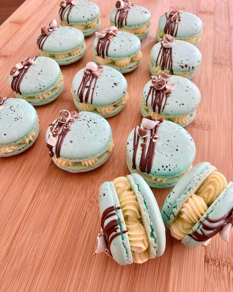 Light blue macarons decorated with chocolate on a wooden table.