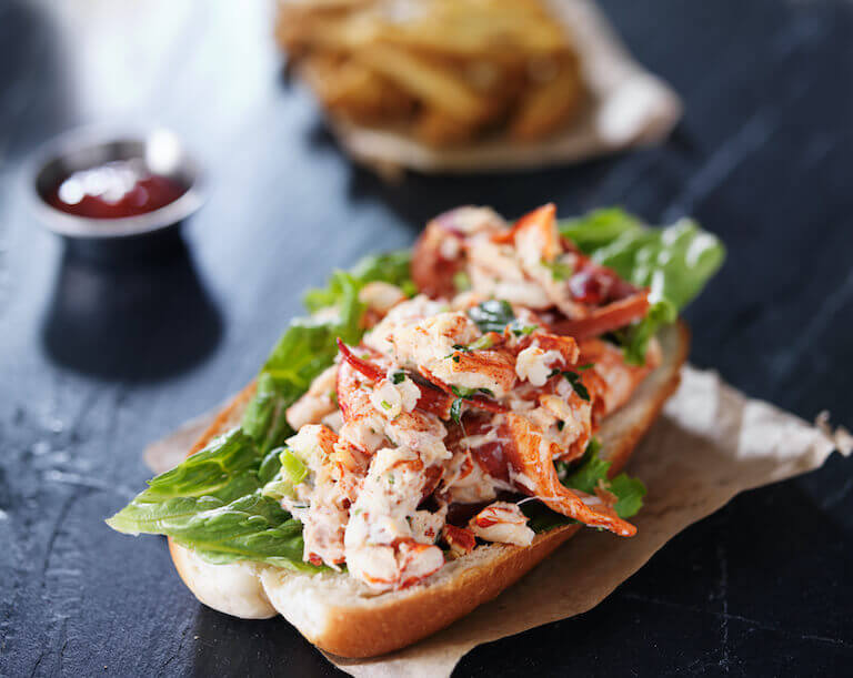 Lobster roll with lettuce on a black slate surface.