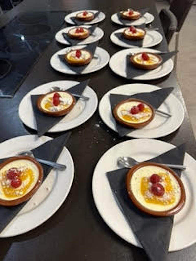 Multiple dessert plates featuring custard tarts topped with fruit, each served with a spoon on white plates with black napkins.