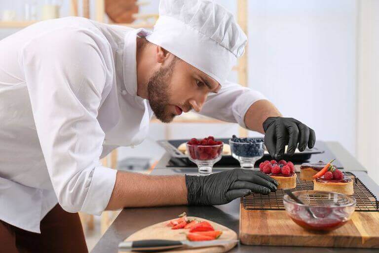 Pastry chef placing raspberries on desserts.
