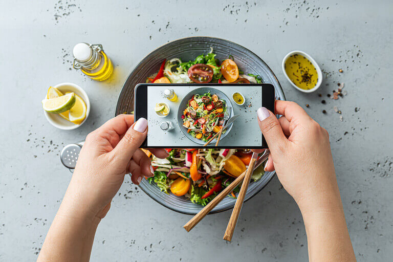Person taking photo of vegetable salad with smartphone