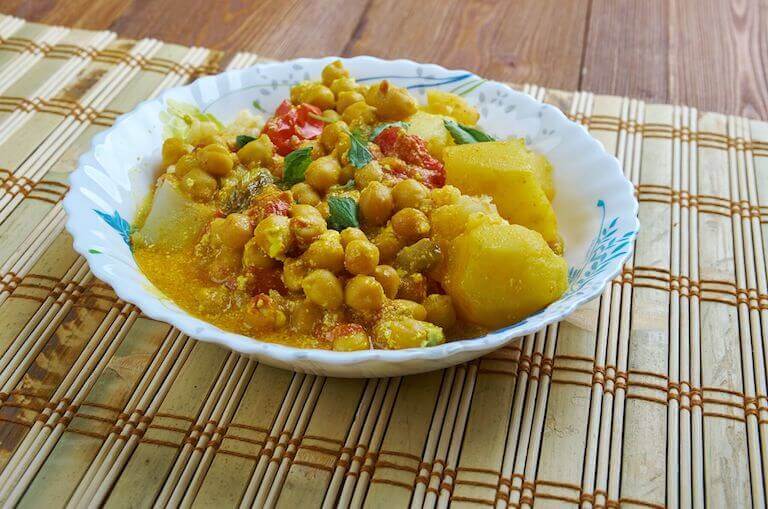 A bowl of chickpea and potato stew in a white bowl on a tan placemat.