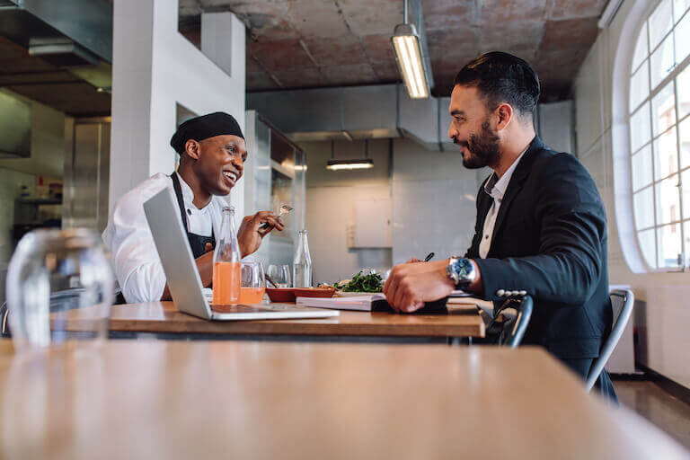 Restaurant manager having a conversation with chef with laptop on table.