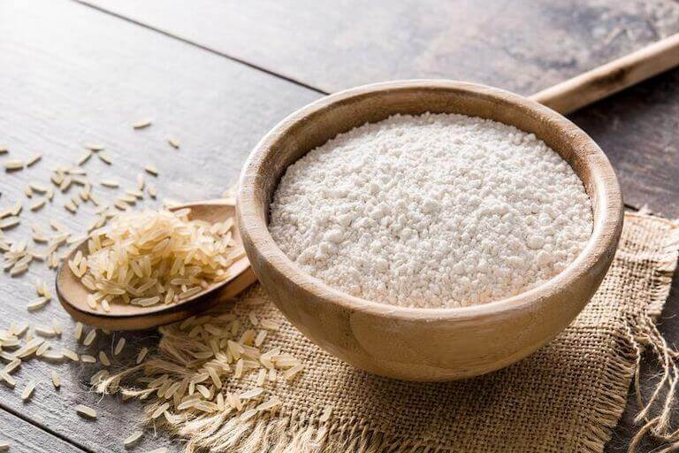 Rice flour in a wood. Bowl next to a spoonful of rice.