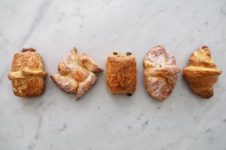 row of crispy, buttery, browned French pastries lie on a white, marble tabletop.