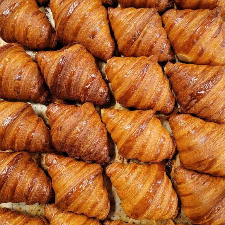 Rows of golden, freshly baked croissants arranged neatly on a baking tray, showcasing their flaky layers.