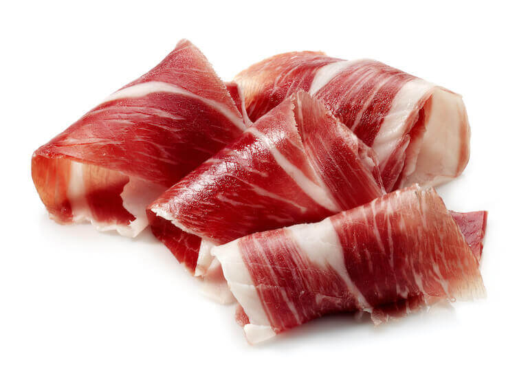 Four thin slices of Iberico ham, rolled, set against a stark white backdrop.