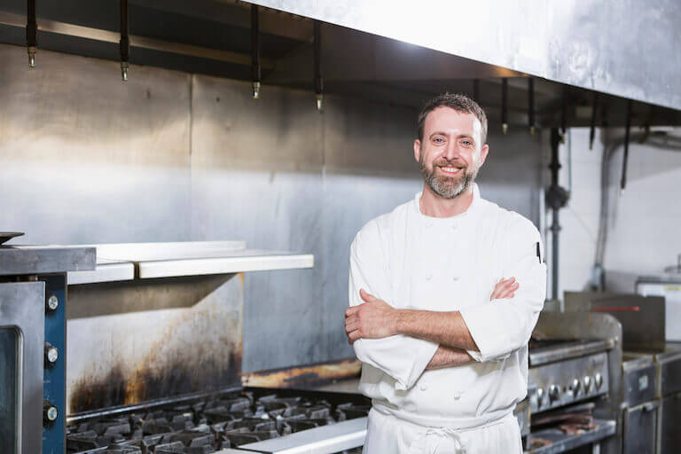 Smiling man with beard with crossed arms in commercial kitchen
