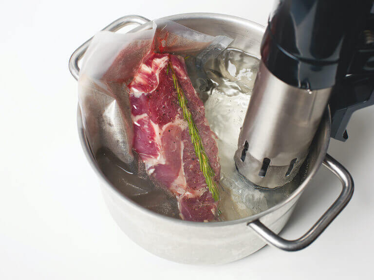 Steak cooking in sous vide water bath with an immersion circulator, illustrating the precision and control of the sous vide technique.