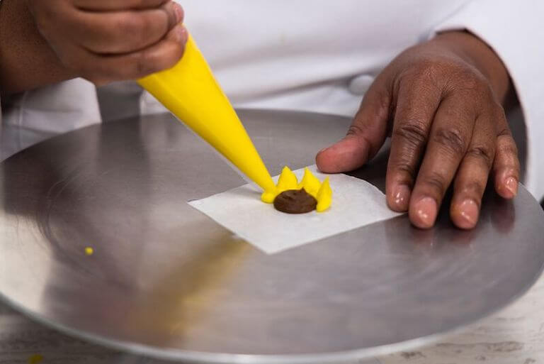 Baker using a plastic pastry bag for an intricate sunflower creation