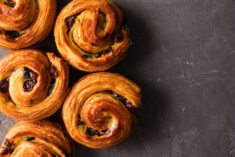 Golden spiral-shaped pain aux raisins on a stone surface, showcasing raisins and flaky layers.