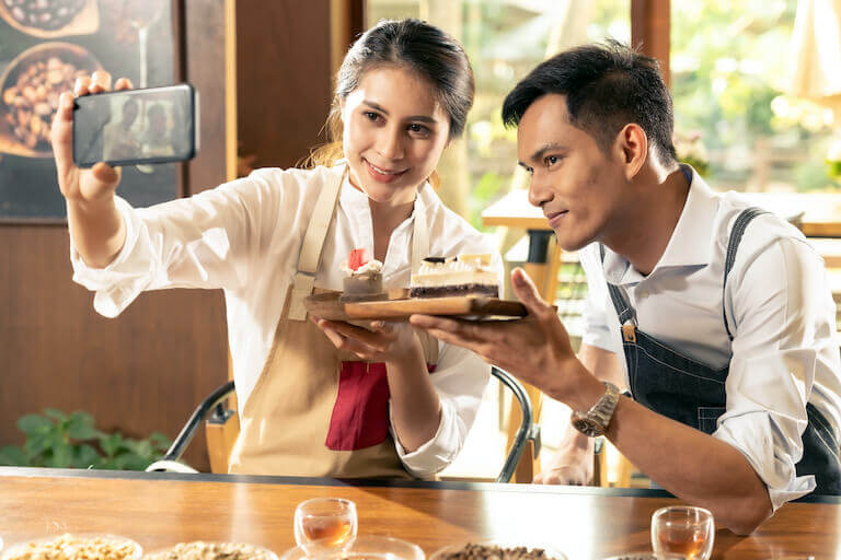 Two employees at a cafe taking a selfie with a pastry.