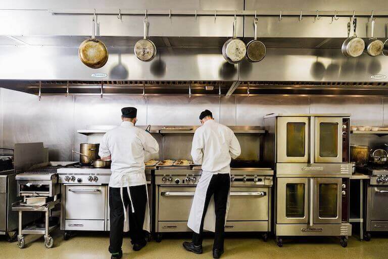 Two Escoffier students with their backs to the camera while cooking on a stove