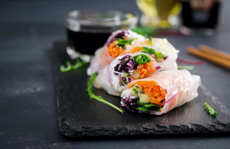 Vegetarian Vietnamese spring rolls filled with carrot, cucumber, red cabbage, and rice noodles, served with a spicy dipping sauce on a wooden surface.