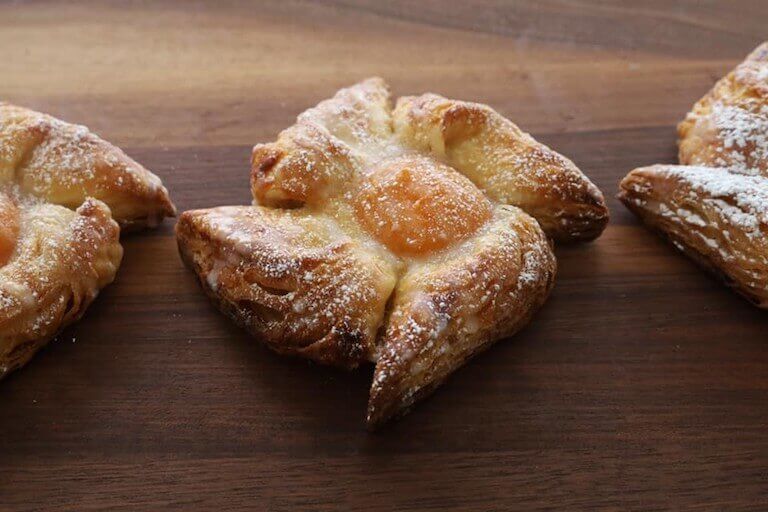 A crispy, brown, pinwheel-shaped pastry with orange jam filling in the center sits on a wooden board.