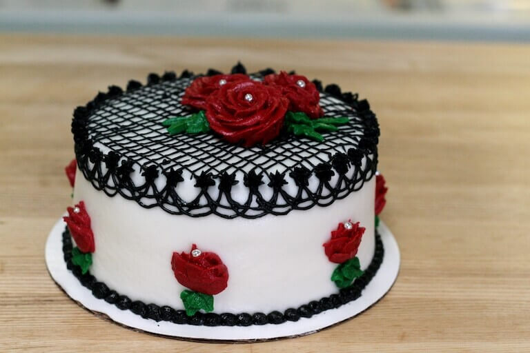 White cake elegantly decorated with black piping in intricate patterns and topped with vibrant red roses, creating a striking contrast.