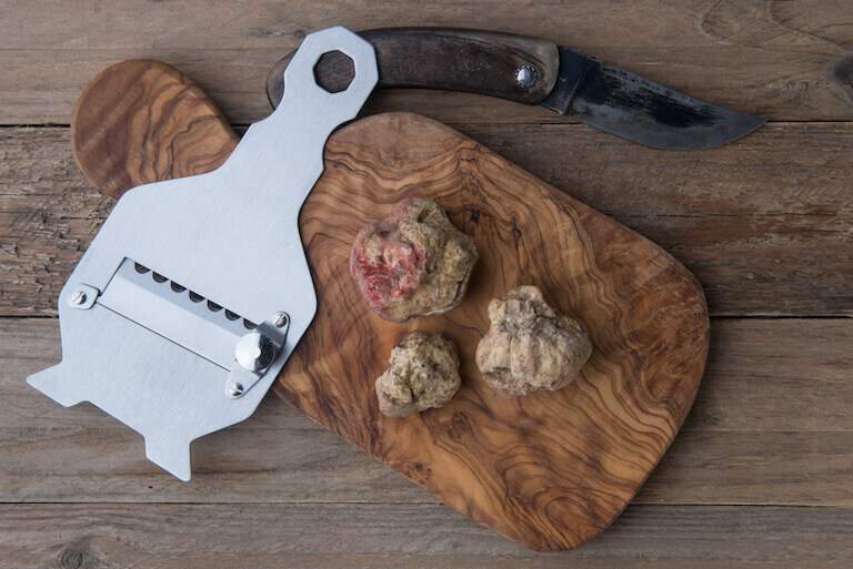 White truffle sits on a wooden cutting board with a special truffle shaver next to it.
