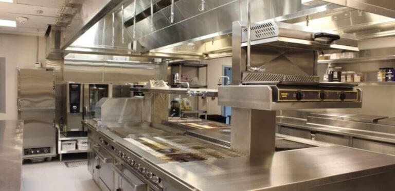A clean, professional-grade commercial kitchen with stainless steel countertops, industrial stoves, and ventilation systems, ready for food preparation.