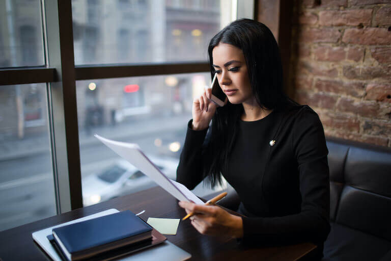 Woman speaking on her cell phone while holding papers in front of her.