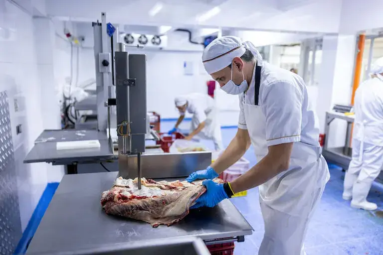 A butcher cuts meat with an electric saw at a butcher’s shop.